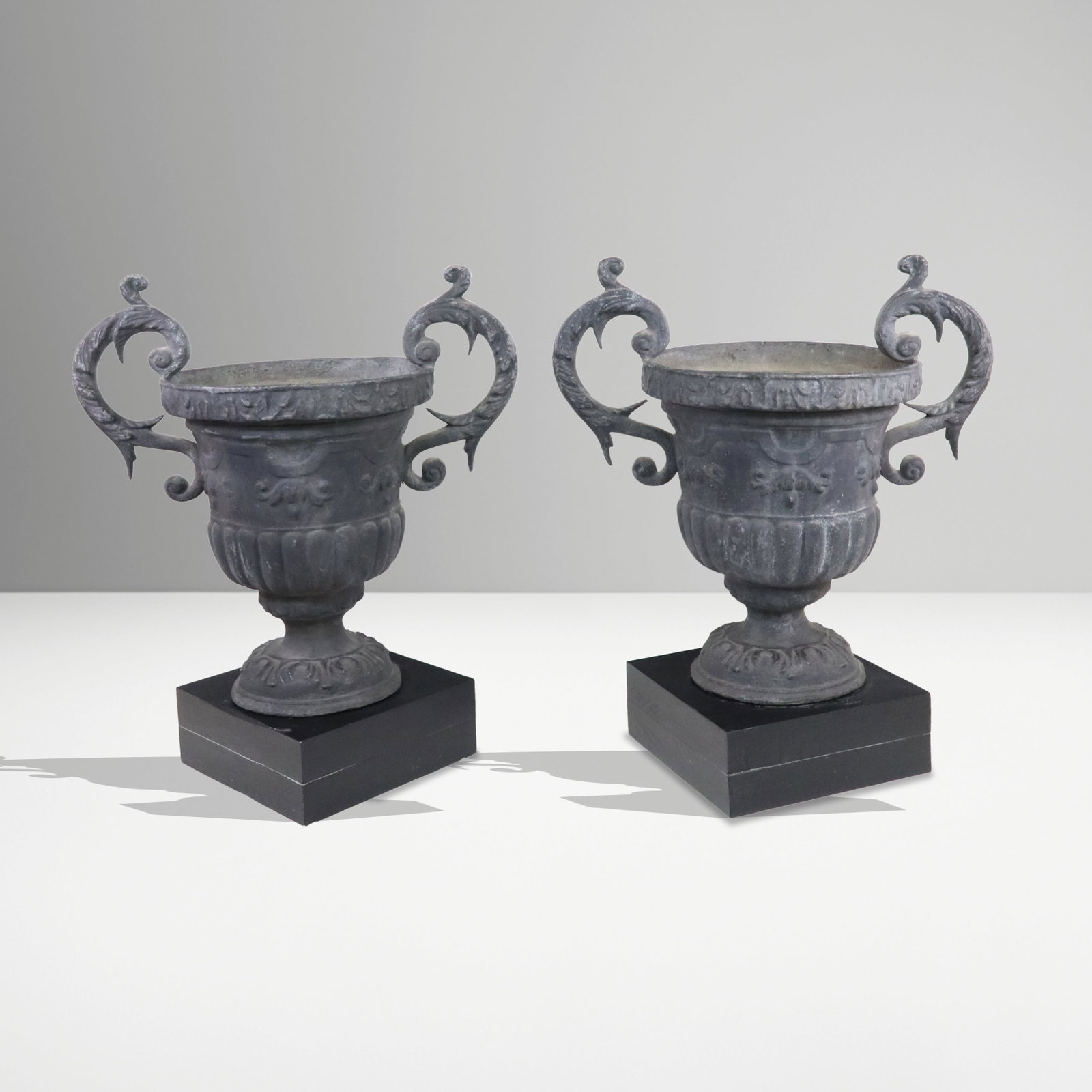 Pair of Neo-Classical Planter Urns: Pair of Neo-Classical manner two handle urns, scrolling handle urns with ribbed and shaped bodies, Zinc / Lead, on square stands. [19" H x 19" W x 12" D; total on stand 22.5" H]. Wear to finish, scrat