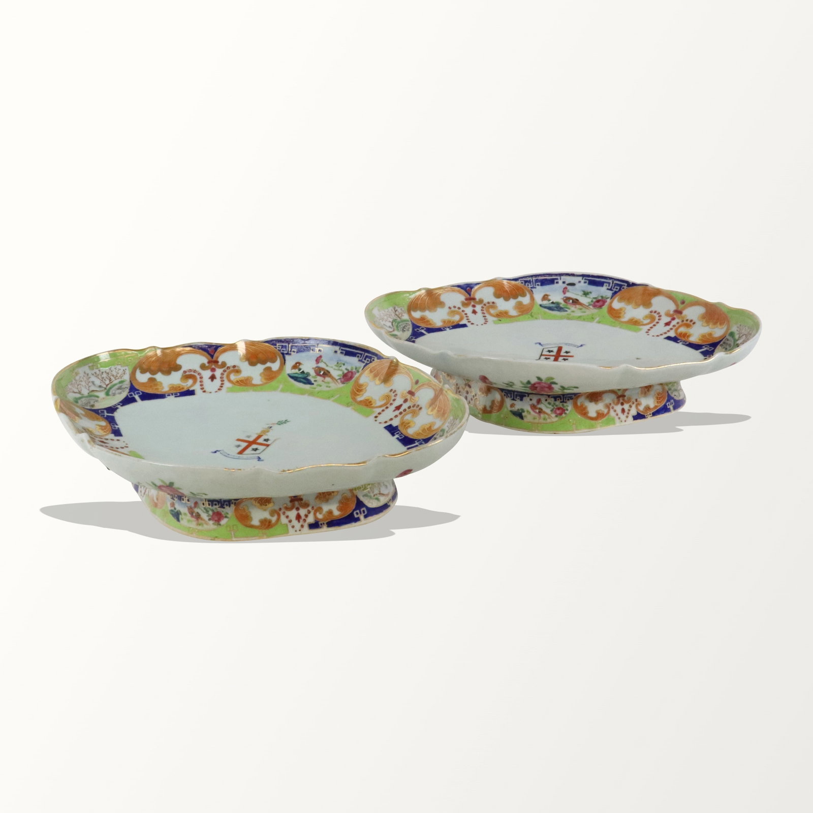 Pair of Chinoiserie Decorated Footed Plates: Pair of chinoiserie decorated footed serving dishes, probably English Ironstone, of navette shape with scalloped border, decorated with vignettes of birds in landscapes, and centering an armorial, in 