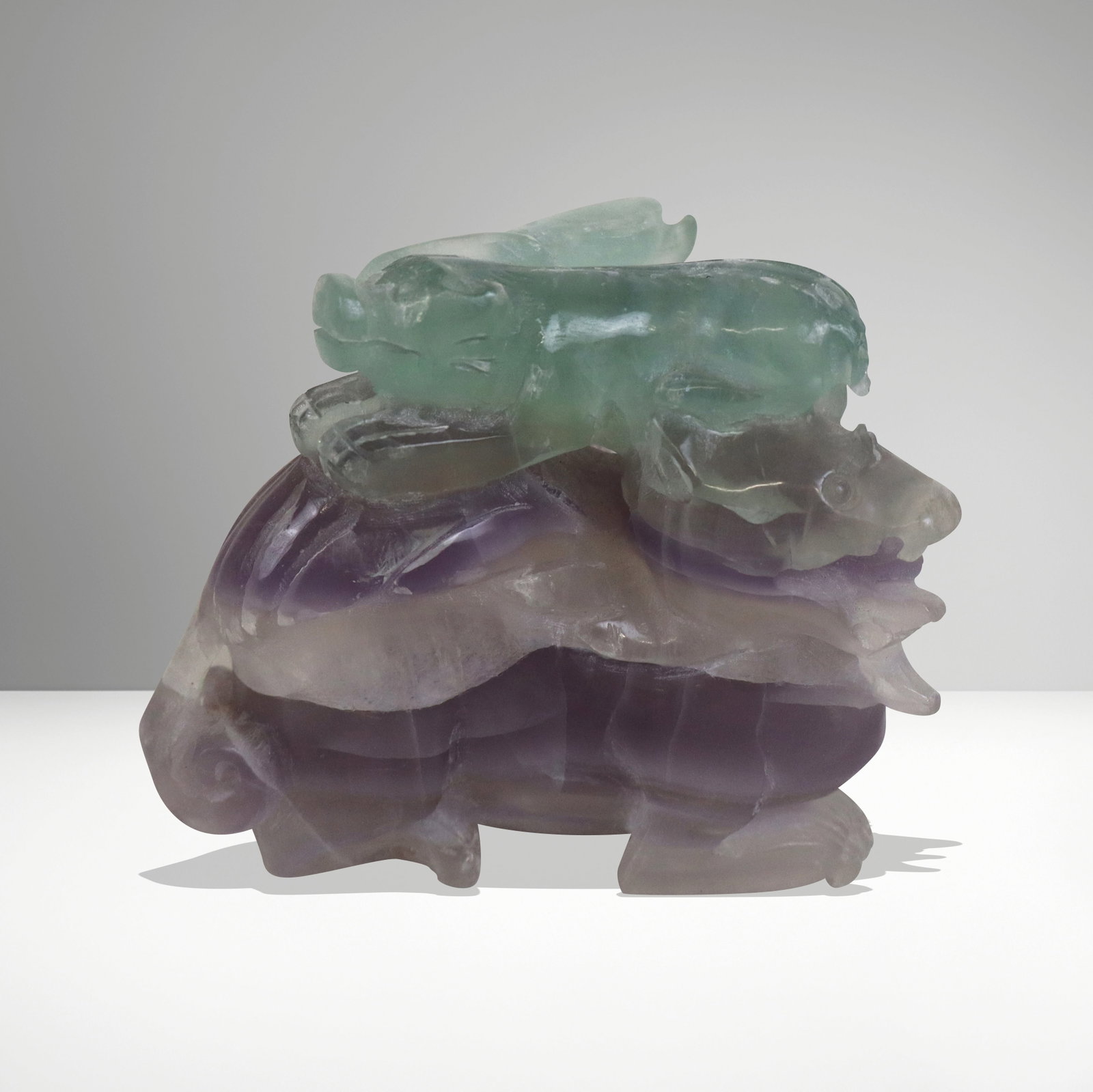 Chinese Carved Fluorite Animal Group: Chinese carved fluorite animal group, early 20th century, 2 tone in purple and green, one animal riding atop a dragon, triangular in shape. [3.5" H x 4" W x 3" D]. Chip and loss on back side, and tail