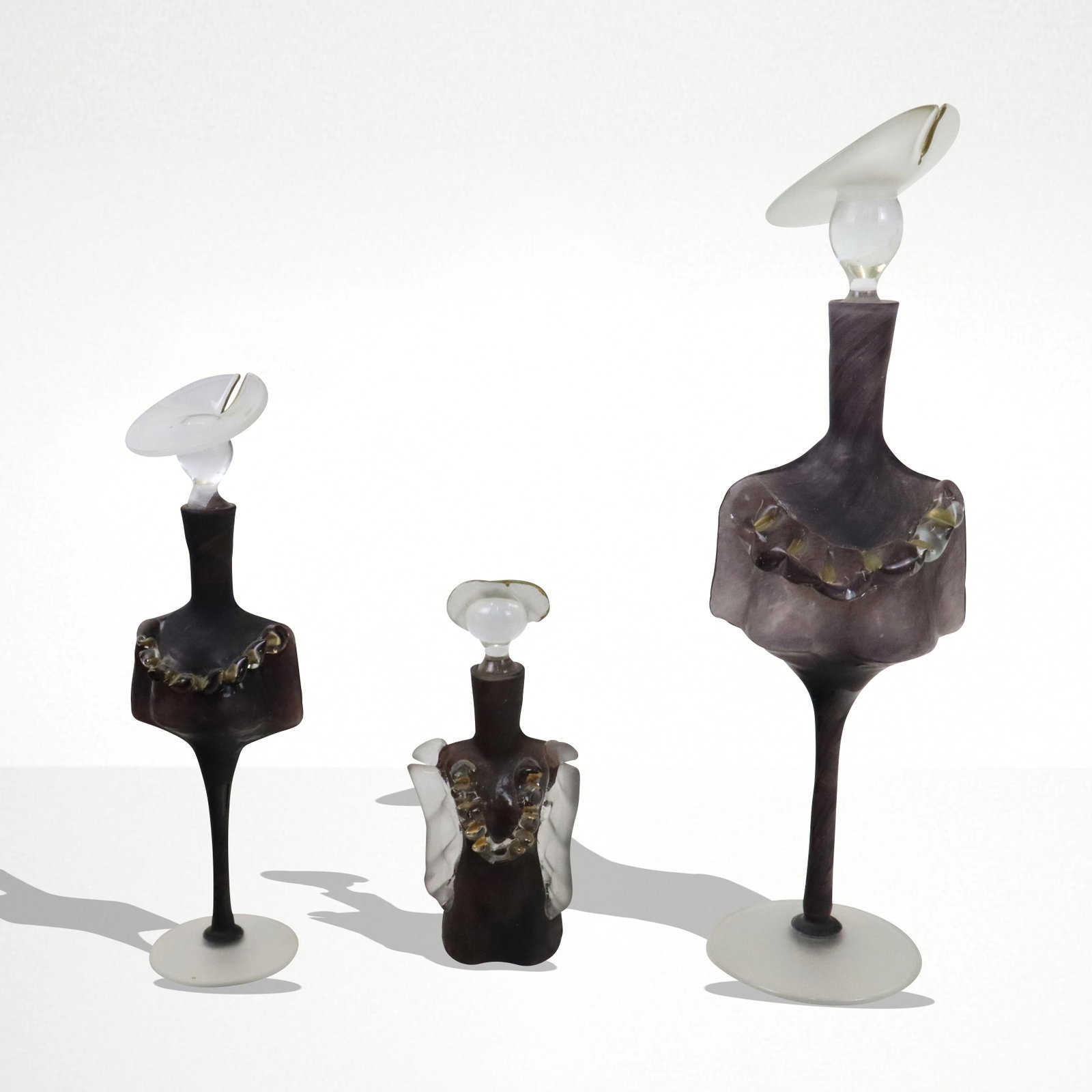 Set of Three Elena Amber Art Glass Figural Perfume: Three Elena amber art glass figural perfumers, each having gilt trim neckline ruffle, one with arms and no stem, different hats. Germany, 20th century. [Tallest 17" H]. Fine condition.