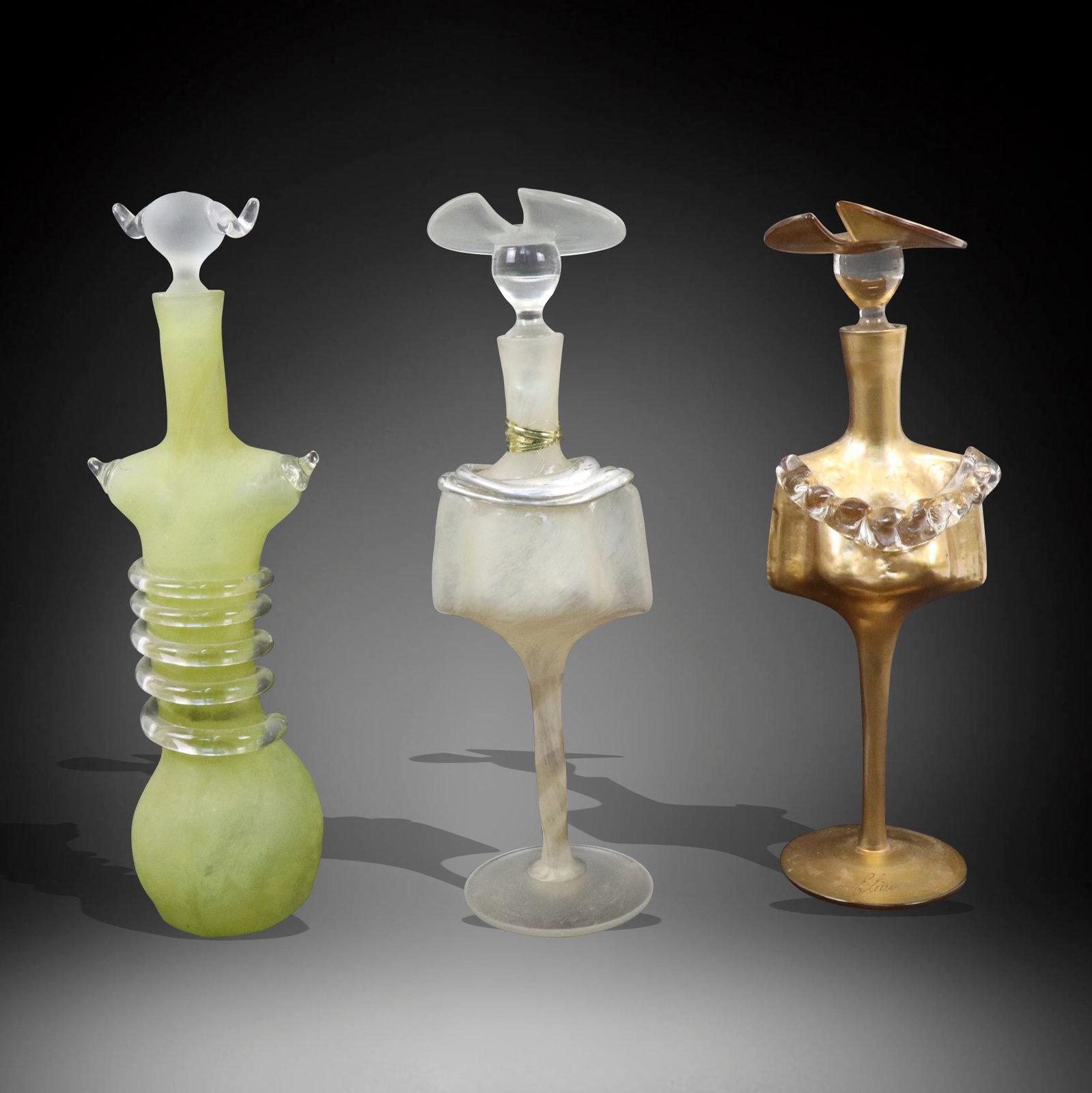 Assorted Elena Art Glass Perfumers, 3: Three assorted Elena art glass perfumers, one rare green and swirl body with unusual head stopper, one frosted, and one gilt. Germany, 20th century. [Tallest 11.5" H]. Green and frosted cannot locate 
