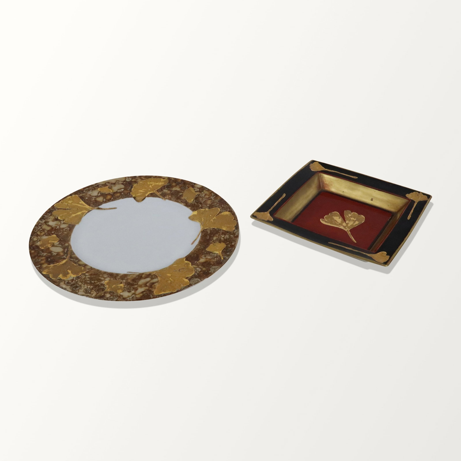 Karin REZA Two Hand-Painted Plates: Karin Reza (Austrian b/French) porcelain hand-painted with gilt Ginko leaves plates, marks and dates to reverse. [Circular plate: 12.75" Diameter, Shallow tray: 8.25" Square]. Overall condition is