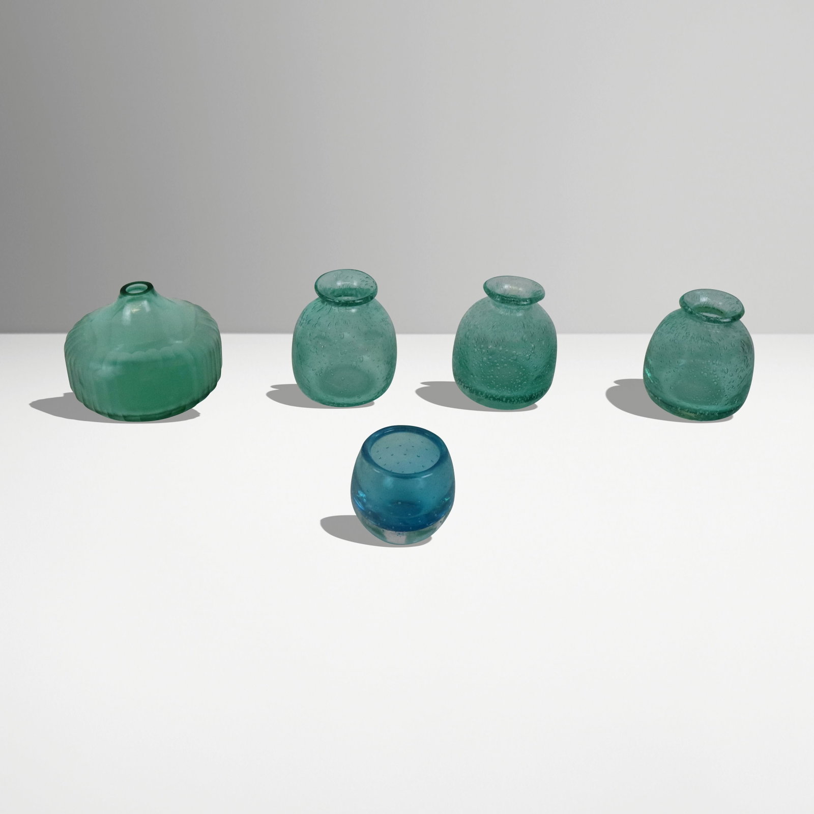 Collection of Blue & Green Glass Vessels, 5: Collection of green bubble glass hand-blown bud vases, a small blue glass votive, and a fluted green glass vase. [Fluted vase: 4.25" H x 5" Diameter]. Overall condition is good.