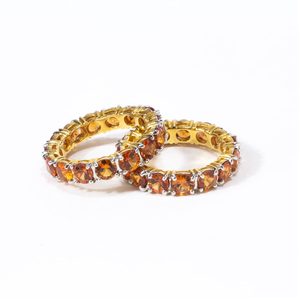 Two Orange Sapphire & Gold Eternity Bands: Two orange sapphire and yellow gold eternity bands, 30 round cut sapphires, total approximately 9.00 cts., marked 18K. [Total 7.04 dwt., Ring sizes: 6.25 and 6.5]. Overall condition is good, with litt