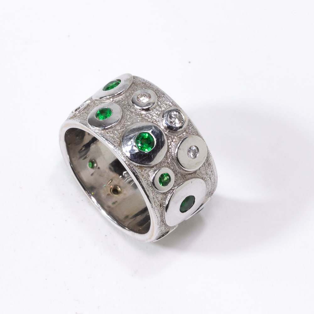 Gold, Diamond and Tsavorite Garnet Ring: White gold, diamond and tsavorite garnet band, designed as wide textured band accented with collect set diamonds and tsavorite garnets, marked on the interior 14K and with makers mark in a line: lips.