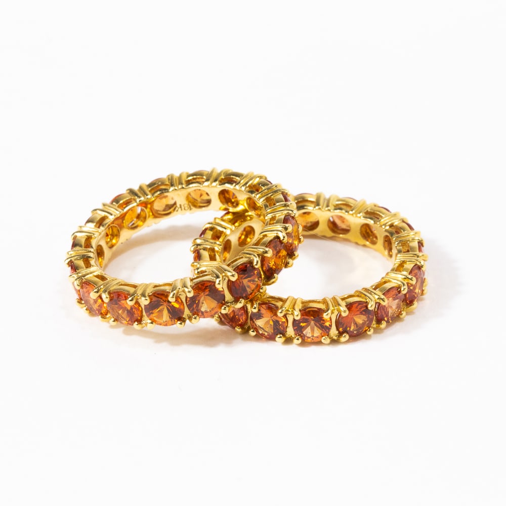 Pair of Orange Sapphire & Gold Stack Bands: Pair of circular-cut orange sapphire and yellow gold eternity stack bands, each containing 16 round sapphires, marked 18K. [Total 7.56 dwt., Ring size: 7.5]. Overall condition is good. From the esteem
