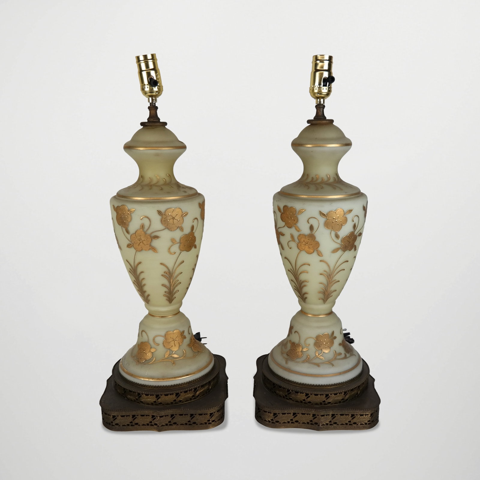 Pair of Opaline Glass Lamps with Gilt Decoration: Pair of opaline glass lamps, 20th century, with hand-applied gilt floral decoration, on reticulated bases. [To socket: 19.5" H x 8.5" Square]. Condition to each is good with some scuffing and patina t