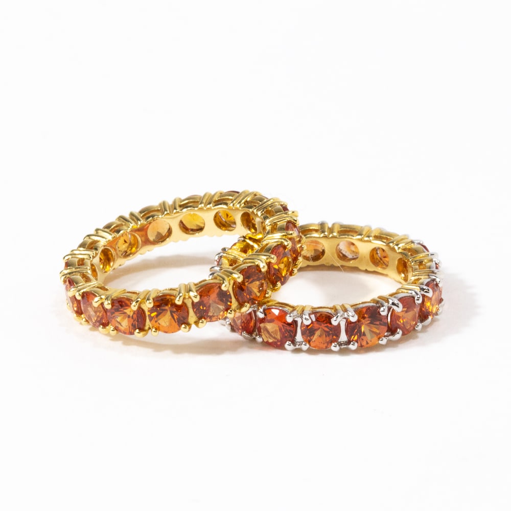 Two Orange Sapphire & Gold Eternity Bands: Two orange sapphire and gold eternity bands, comprising a sixteen stone orange sapphire band in yellow gold, and a fifteen stone orange sapphire band in yellow gold with white colored gold prongs, eac