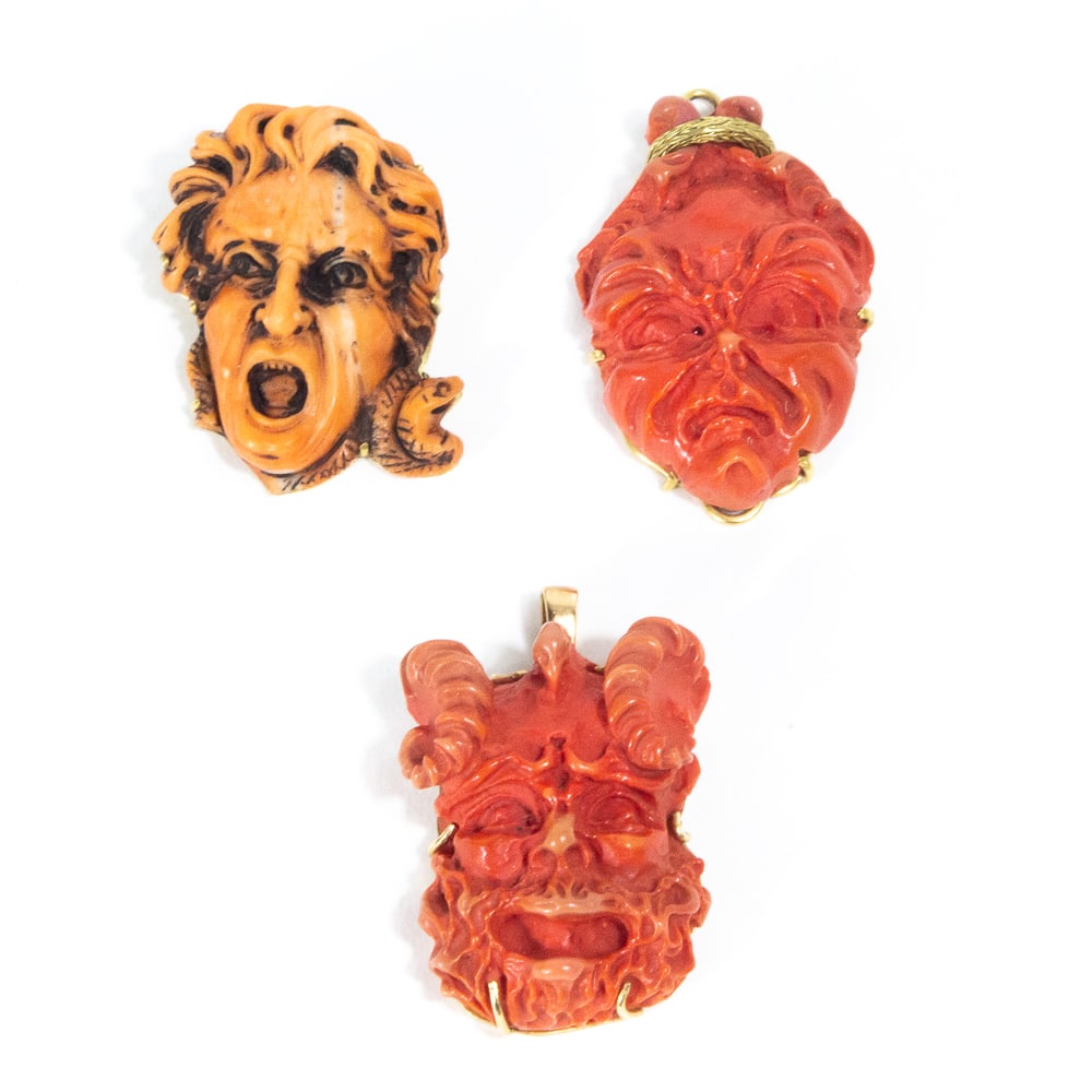 Three Carved Coral & Faux Coral Pendants: Three carved coral and faux coral pendants with gold mounts, comprising a coral head of Medusa, a faux coral grotescue face of Pan with curved goat horns, and faux coral scary face, unmarked or illegi