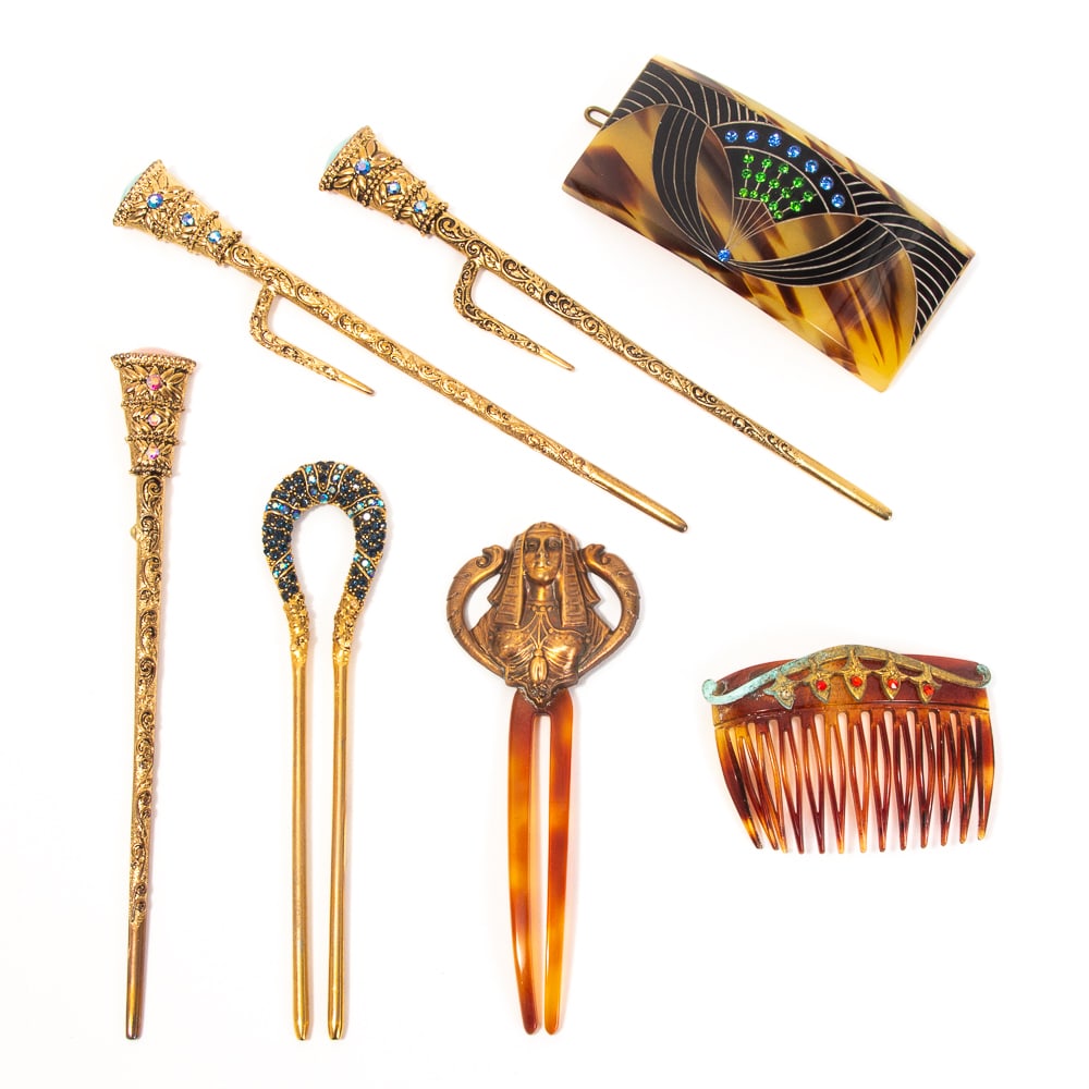 Group of 7 Egyptian Revival Hair Combs: Group of seven Egyptian Revival hair combs, late 19th-mid 20th century, including an Art Deco barrette with blue and green faux gems set within a winged motif, a metal relief hair pick depicting a por