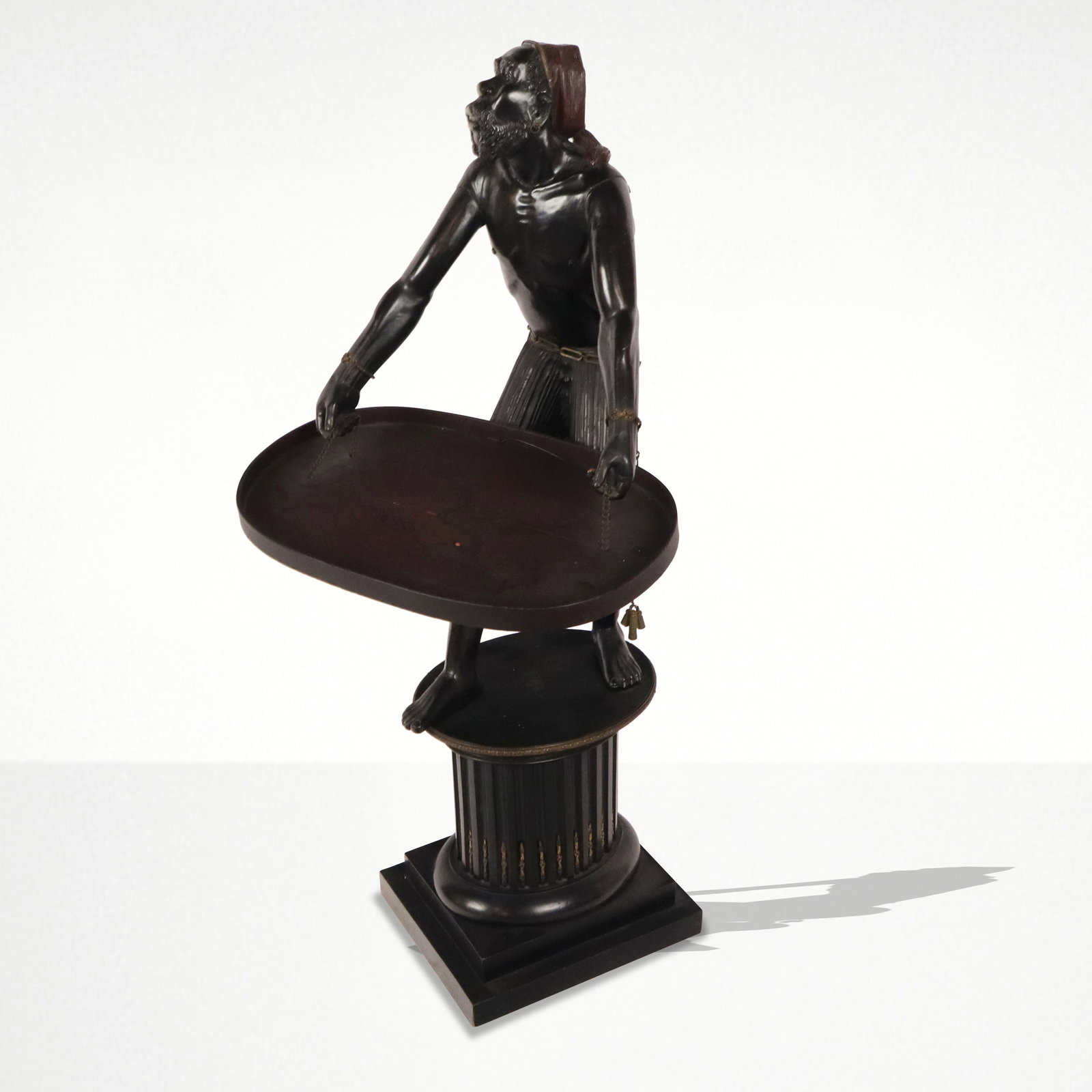 Carved Wood Blackamoor: Carved wood Blackamoor sculpture, Italy, 19th century, with a figure holding a chinoiserie decorated tray suspended on chains, on a carved wood and bronze mounted pedestal base. [45" H x 20" W x 22" D