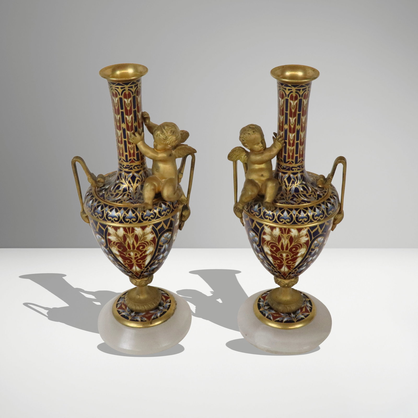 Two Champleve Enamel Vessels: Two champleve enamel vessels, probably French, 19th/20th century, comprising a small baluster form vase on onyx base [6.25" H x 3" Square], and small pierced vessel held / carried by three putti [3.5"