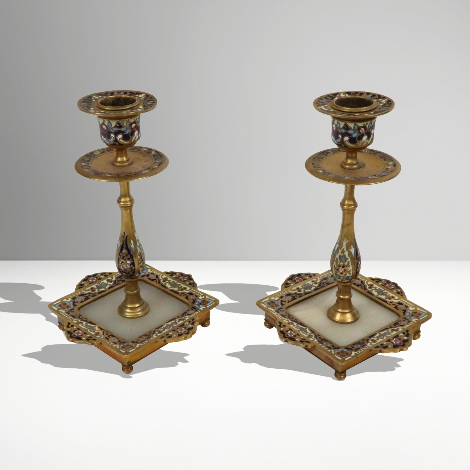 Pair of Champleve Enamel, Onyx and Bronze Candelst: Pair of champleve enamel, onyx and bronzer candlesticks, French, probably first half of the 20th century, the bobeche, capital and drip pan, baluster form column and base with bands of champleve ename