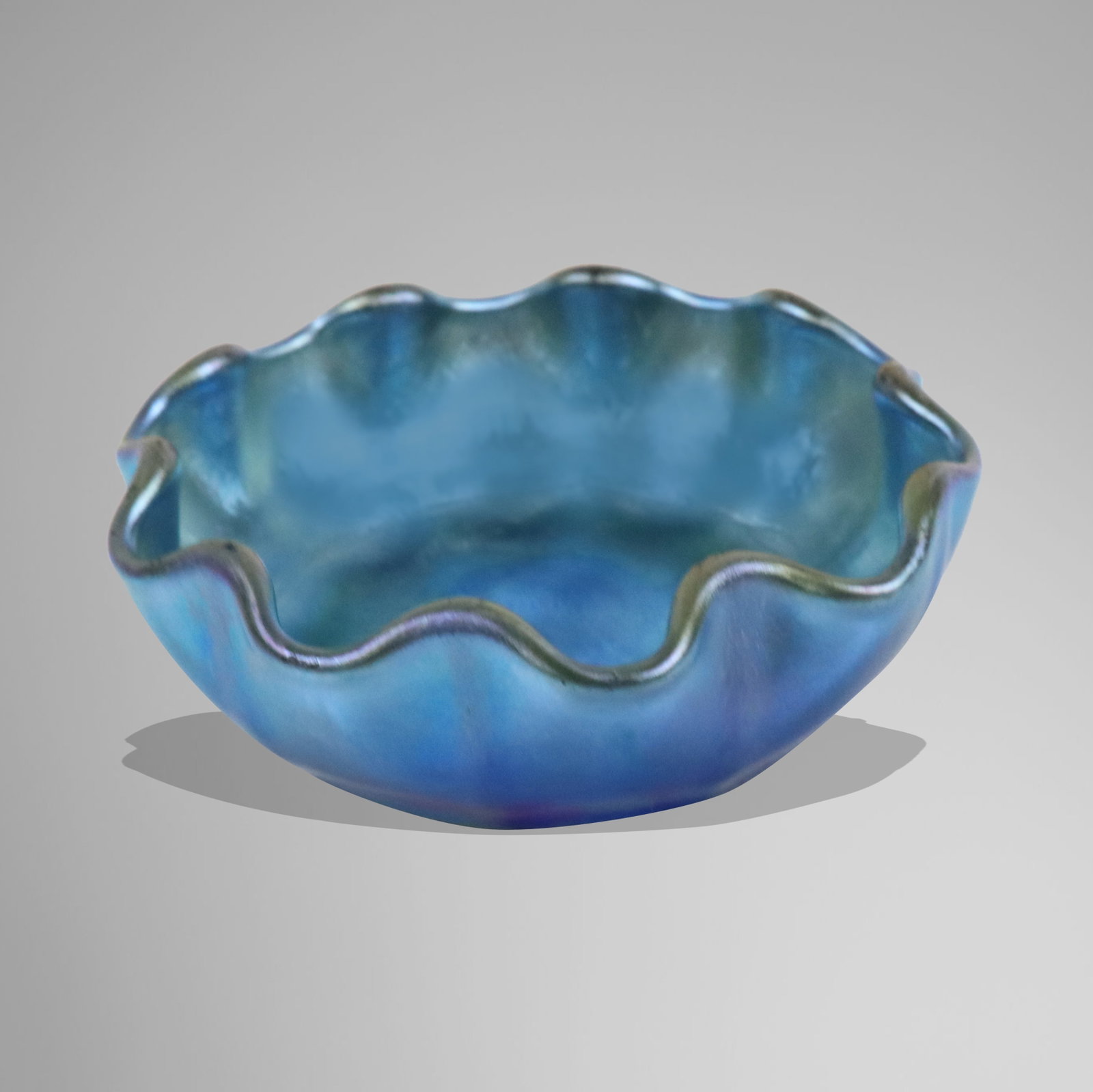Tiffany Studios Favrile Glass Salt Cellar: Louis Comfort Tiffany iridescent blue Favrile glass salt cellar, first quarter of the 20th century, the shallow bowl with wavy rim in shades of light blue turning to dark blue and them purple, etched 