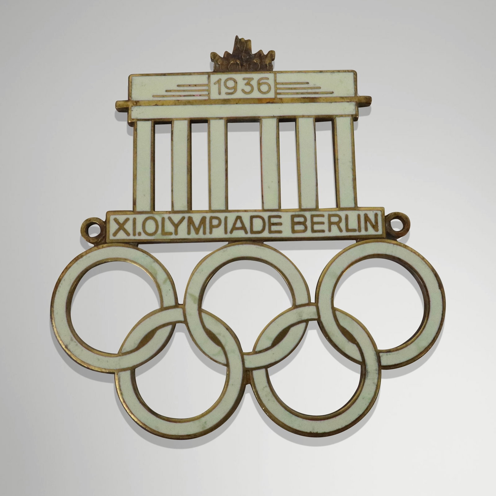 German Enamel 1936 Olympic Badge: Original white enamel German 1936 Olympic badge. Provenance: From the Estate of Dr Robert Reber, Greenwich, CT. [3" x 2.75" W].