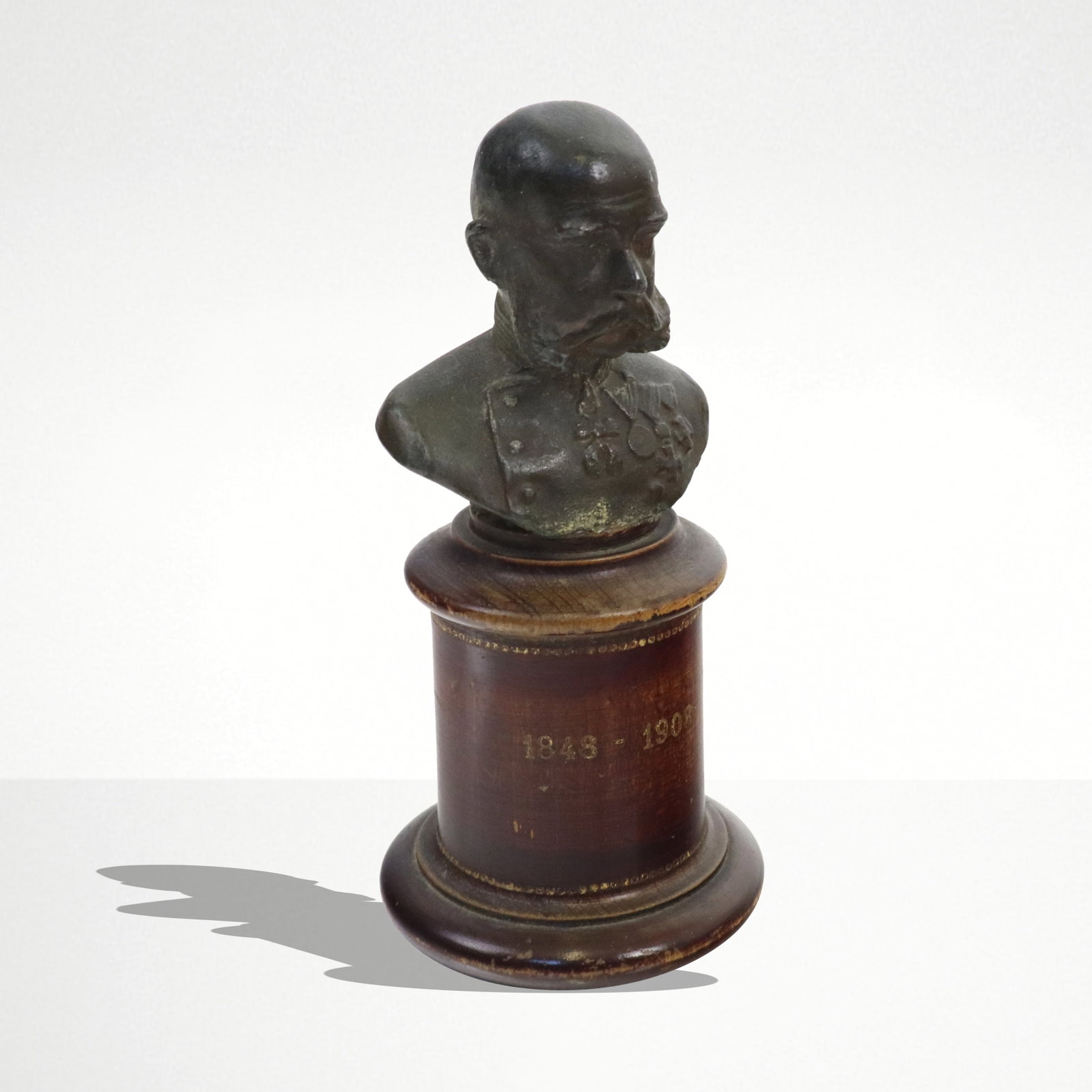Franz Joseph Bronze Bust On Pedestal: Miniature bust commemorating the Jubilee of Franz Joseph of Austria, 1848-1908, in bronze on wood pilaster. Provenance: From the Estate of Dr Robert Reber, Greenwich, CT. [4" H].