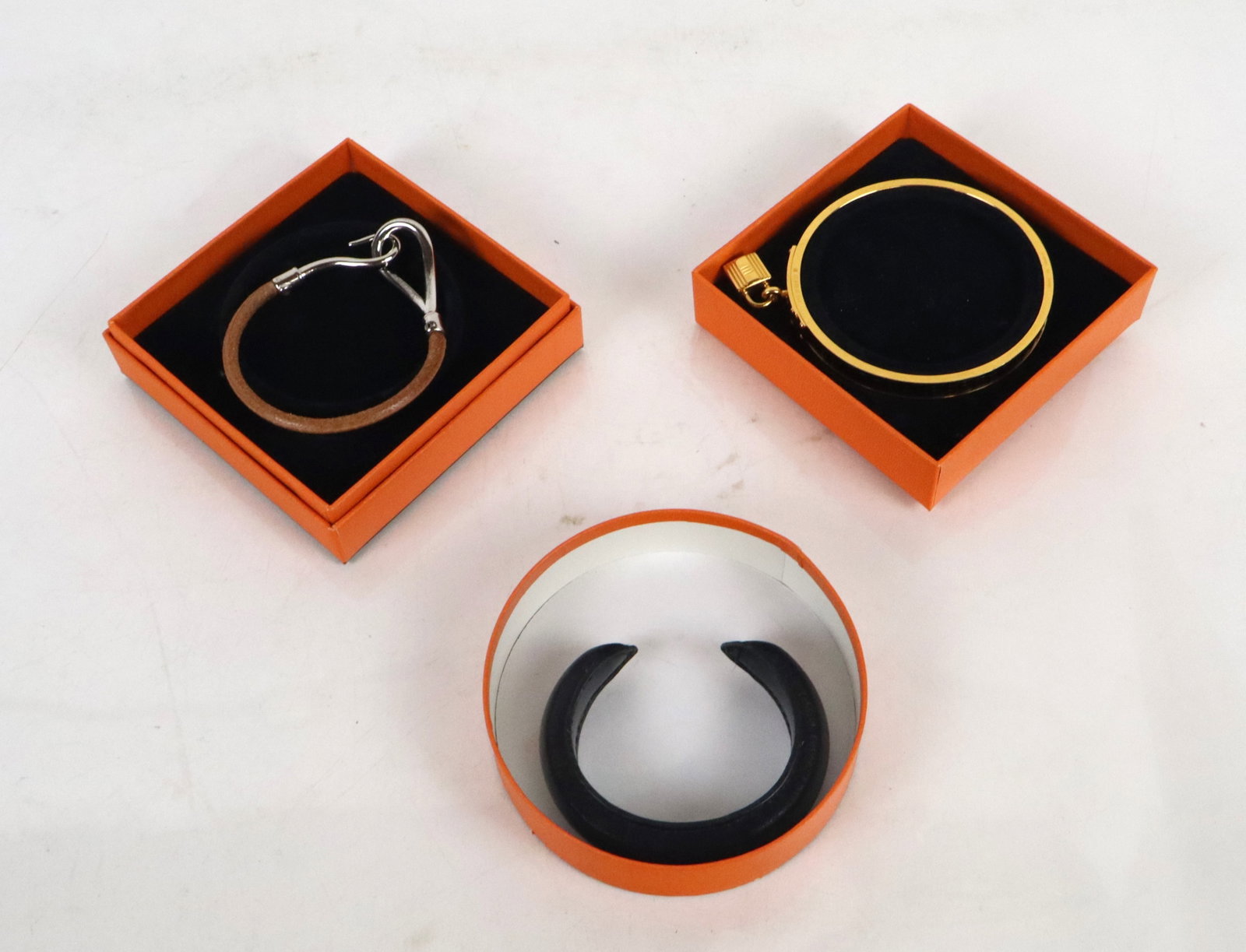 Hermes Group of Three Bracelets: Hermes group of three assorted bracelets, comprising a narrow rigid cuff [Interior 5" L x 5/8" W], leather and stainless hook bracelet [7" L overall], and gold-tone metal and leather Cadena brangle br