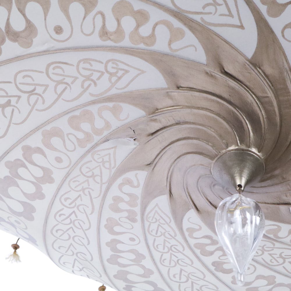 Fortuny "Scudo Saraceno" Silk Chandelier Shade: "Scudo Saraceno" silk chandelier shade by Mariano Fortuny, Italy, 20th/21st century, in gilt printed silk, with an interior acrylic shade, and blown glass pendant, unmarked. [Shade, less hanging imple
