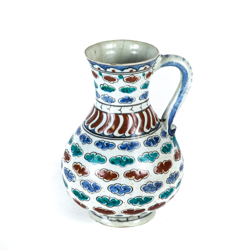 Antique Iznik Pottery Jug: Antique Iznik pottery jug, possibly Ottoman Turkey, of baluster form resting on a short foot and with slight flaring lip and shaped handle, decorated with bands of clouds in blue, green and red, the n