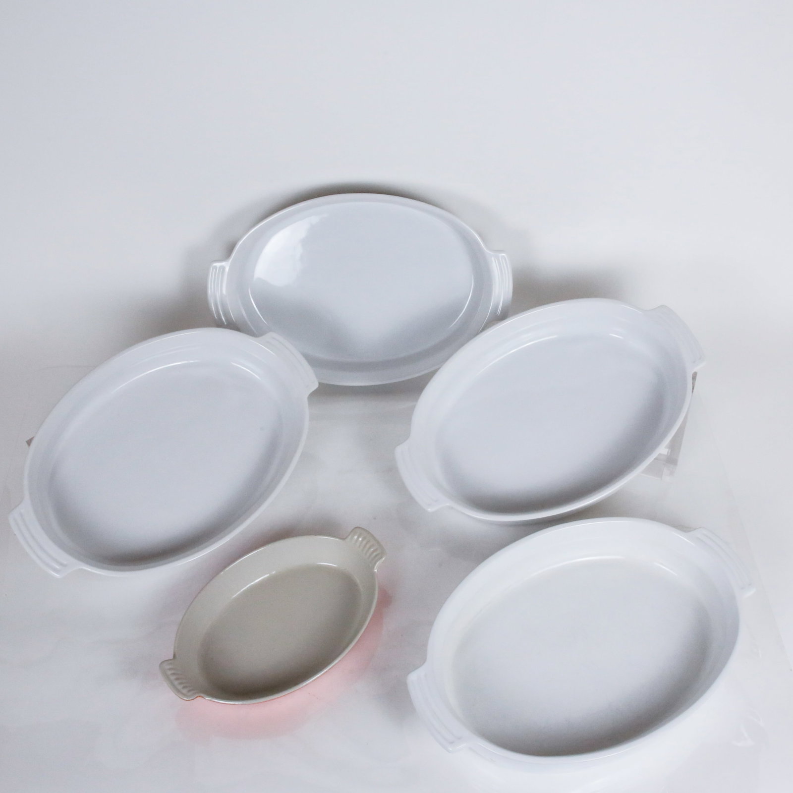 Le Creuset Casserole Dishes, 5: Le Creuset set of four white oval two handled casserole or baking dishes [2.5" H x14" L x 10.5" W], and a small orange a gratin dish [11" L x 7" W], mark to underside of base. Overall condition is