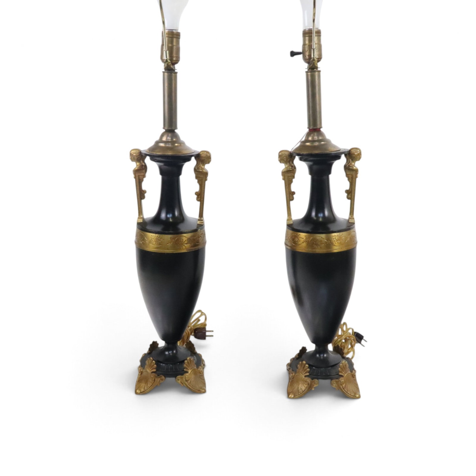Pair of Empire Ebony & Gilt Lamps: Pair of Empire ebony and gilt decorated lamps, 19th century, having a black and gold two-tone patina, on shield-form legs, with faces as handles. [25.5" H to sockets; Bases: 5.5" x 5.5"].