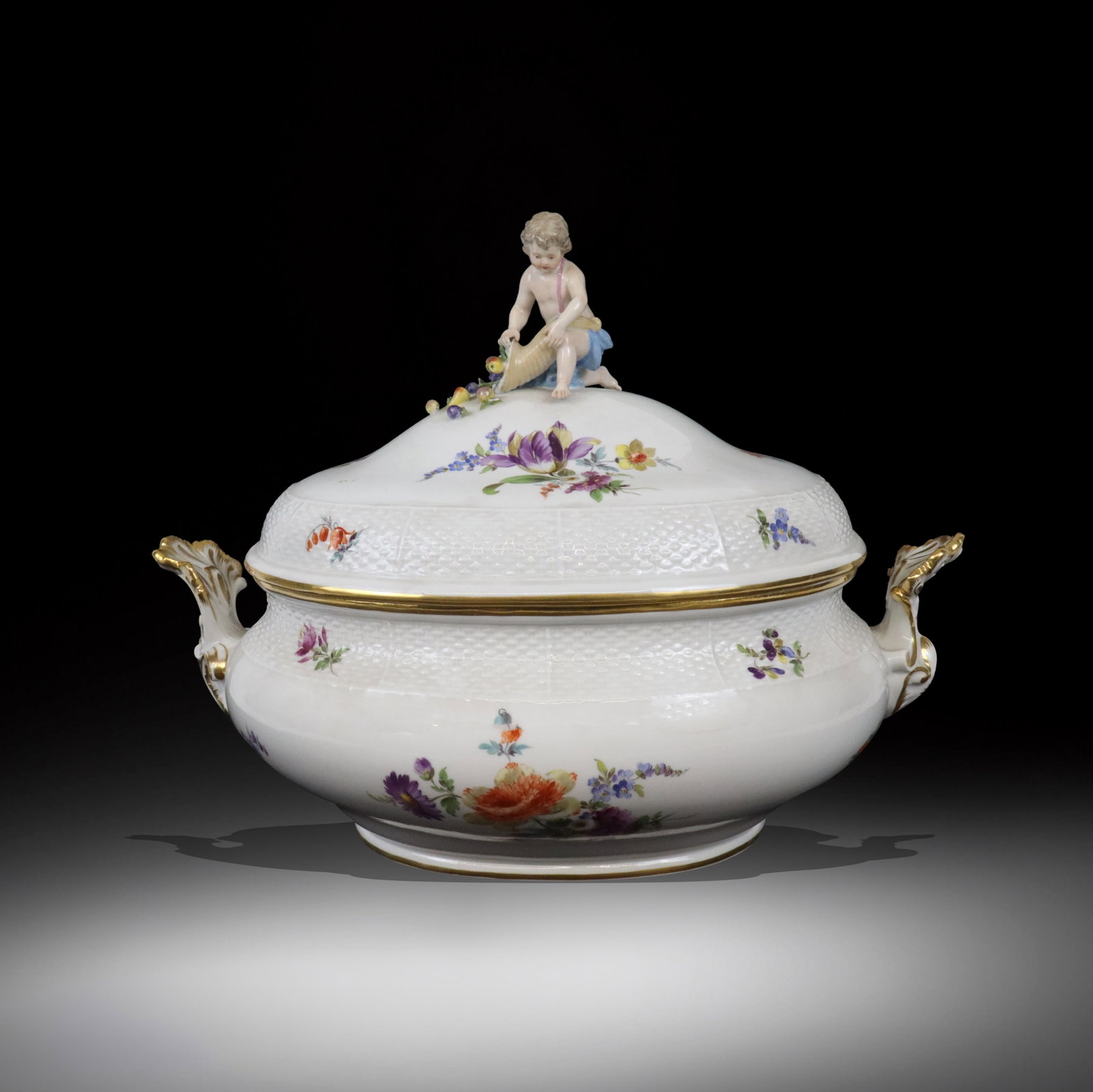 Meissen Floral Basketweave Covered Tureen: Meissen floral and figural decorated covered tureen, probably German, the white ground with floral decoration and basketweave banding, surmounted by a kneeling lad with cornucopia, mark to base possib