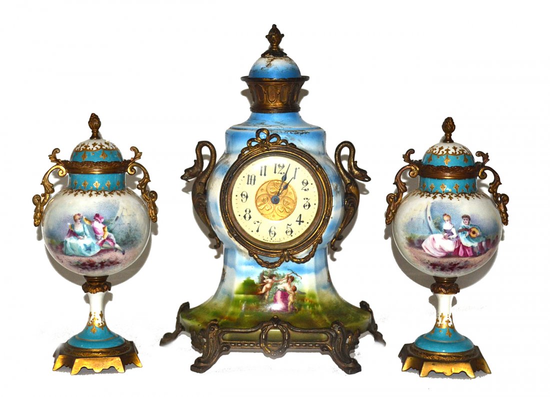 Assembled Continental Porcelain Mantle Clock Set: Comprises a German transferware clock with parcel gilt mounts, accompanied by a pair of hand-painted French covered urns. Clock [9 7/8" W x 5 1/4" D x 13 5/8" H]. Urns [4 3/4" W x 4 1/4" D x 10" H]. A