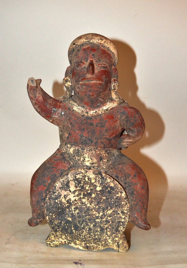 Pre-Columbian Figural Earthenware Vessel: Meso-American earthenware vessel of a musician, depicting a drummer seated on top of a large drum. Losses and wear. Figure's cape broken from shoulders. Sold "as is". 7 1/8" w x 6" d x 12 1/2" h.