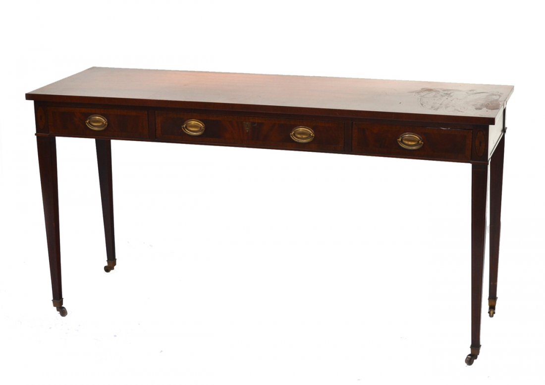 Sheraton Style Mahogany Console Table: Features brass bale handles, banded inlay and tapering legs with brass caster sobot feet. Bears three drawers. Light wear.