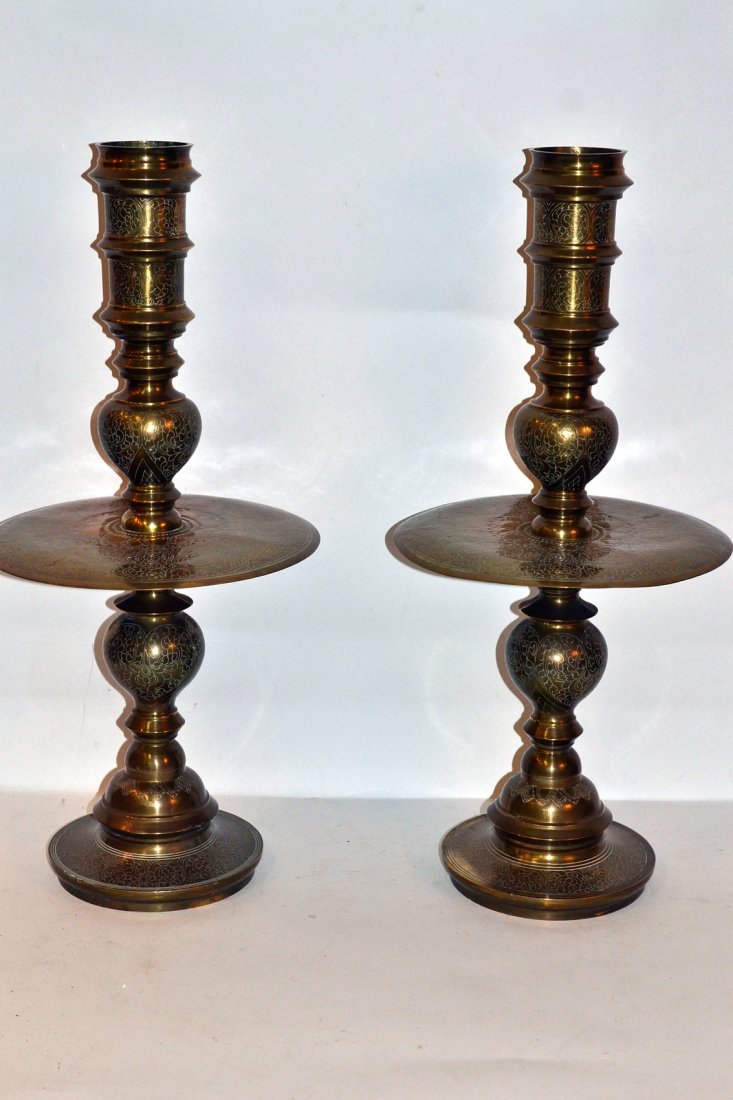 Pair of Dutch Brass Altar Candlesticks: Pair of balustrade form candlesticks with wide under plates and all over incised scrolling tendril decor. [12 1/4" dia x 26 1/4" h]. Each receive [3" dia] candles.