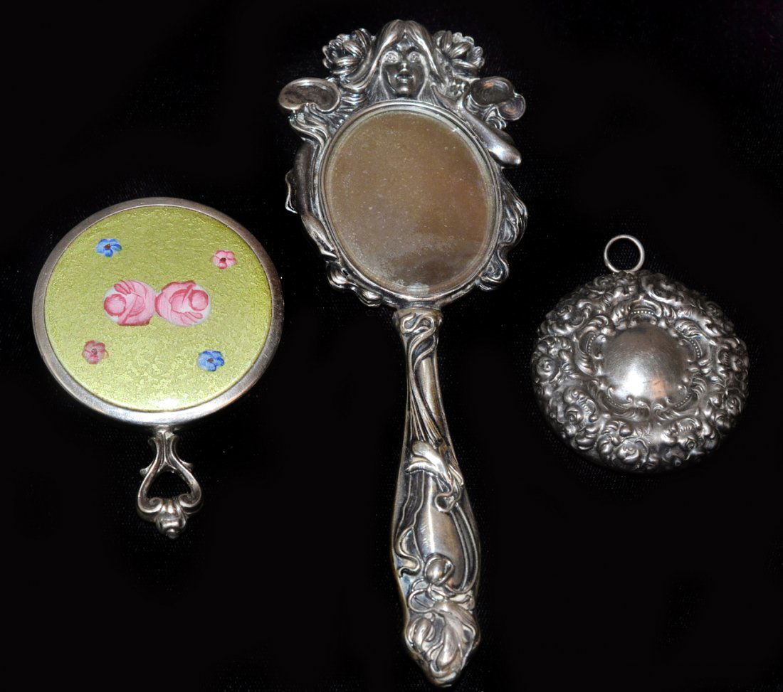 Three Sterling Mirrors: The first, a finely decorated hand mirror in the Art Nouveau taste, early 20th century; the remaining two small circular pocket mirrors. [Largest 6 1/4"]. All in good condition.