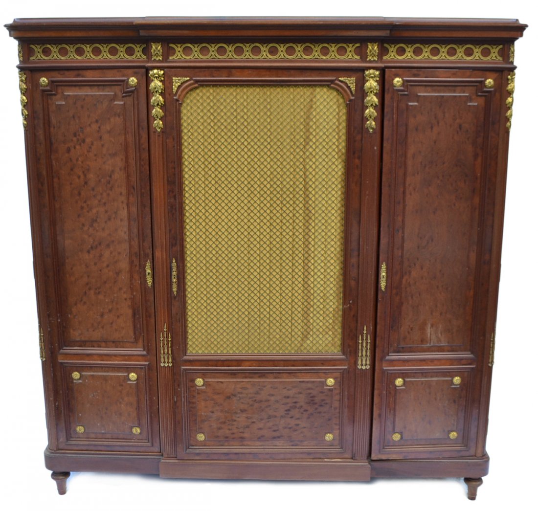 Louis XVI-Style Walnut Cabinet: Bears bronze grille center door flanked by two cabinet doors concealing interior shelves. Features fluted vertical supports occupied by gilt bronze leafy accents and rosettes throughout. [65 3/4" W x 
