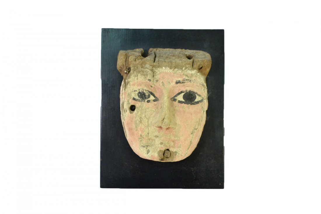 Ancient Egyptian Funerary Mask: Carved and polychromed wood mask bearing five through-tenon holes (two with tenons intact). [4 1/4" W x 2 1/8" D x 5 3/4" H]. Mounted on an ebonized wood stand with hinged strut [8 1/4" H]. Wear with 