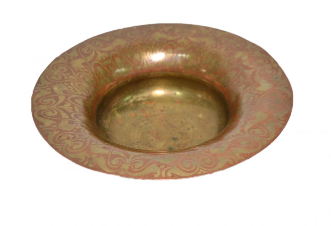 Tiffany Studio New York Bowl: Copper centerpiece bowl with wide flared rim and brass dinanderie scrolling design. Stamped on bottom "Tiffany Studio New York". [11 3/4" Dia x 3 3/8" H]. Shallow dents on rim.