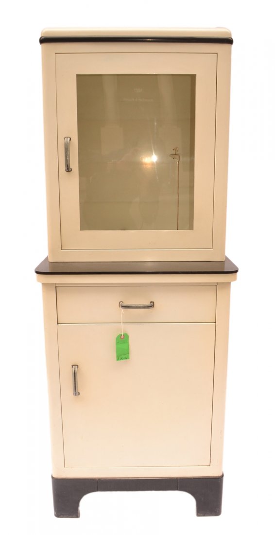 Vintage Medical Cabinet: Creme and black metal cabinet. Bears one top door and one lower door with drawer. [23 1/2" W x 17 1/4" D x 60 1/2" H]. In good condition.