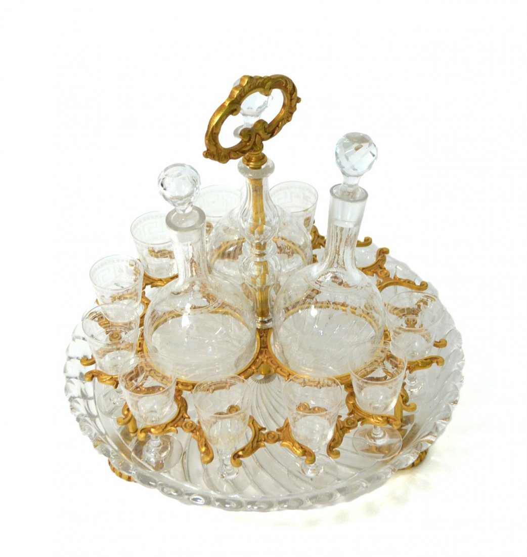 Gilt Metal and Crystal Liqueur Set: Comprised of a circular gilt metal and molded crystal stand, mounted with three etched crystal liqueur bottles and 10 matching stems. Missing two stems and with one replaced stopper. [11" H].