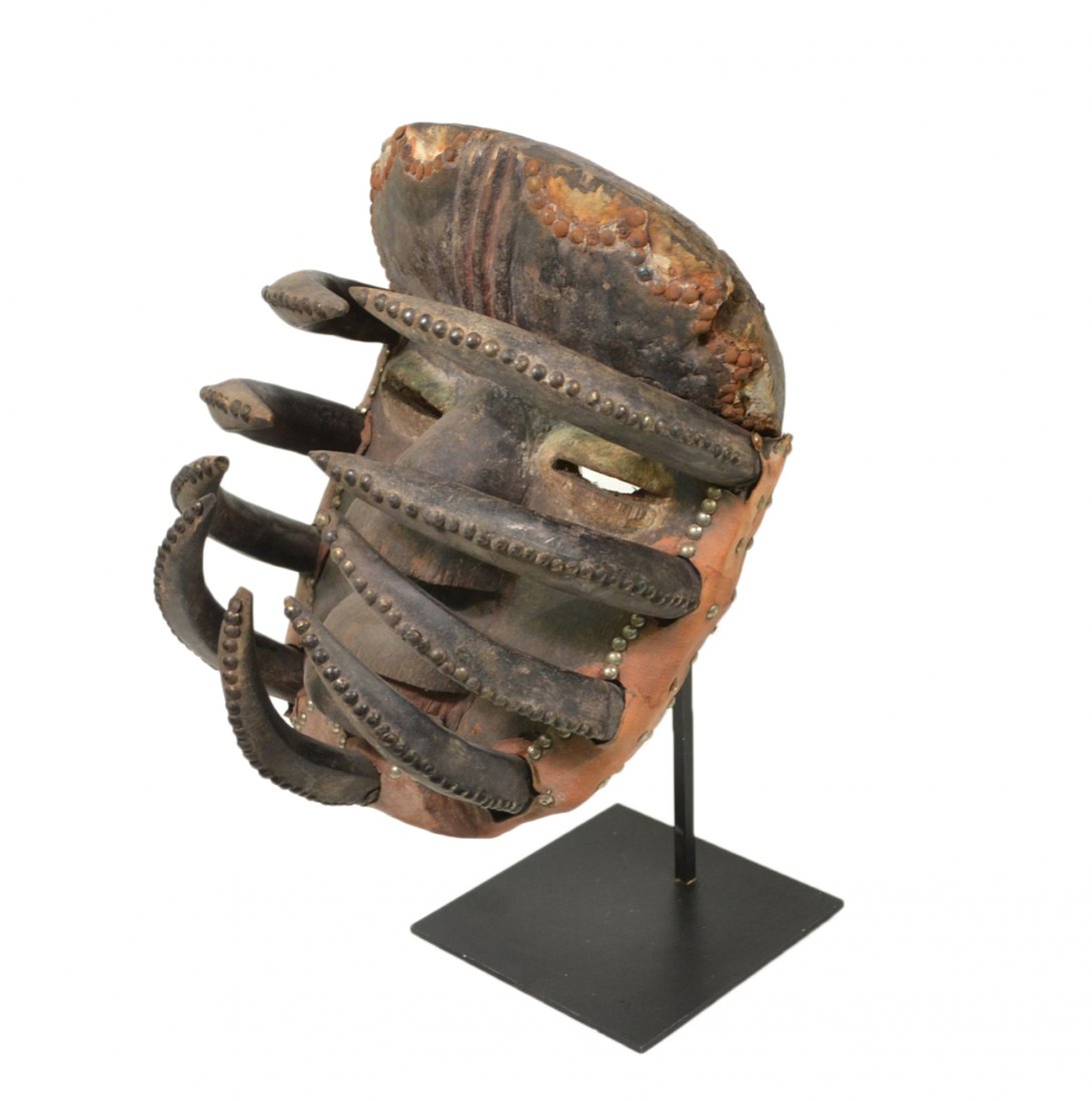 African Tribal Wood Mask: Painted carved wood mask with nine insect-like appendages and leather strap. On custom stand. [11" W x 14" D x 17" H]. Wear commensurate with age.