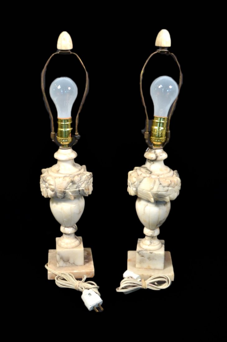 Pair Alabaster Lamps: Pair of alabaster lamps with floral ornamentation along lamp atop urn shape on a plinth base. Urn is loose on one lamp; both lamps have been repaired near base. Wiring has not been inspected. Fair con