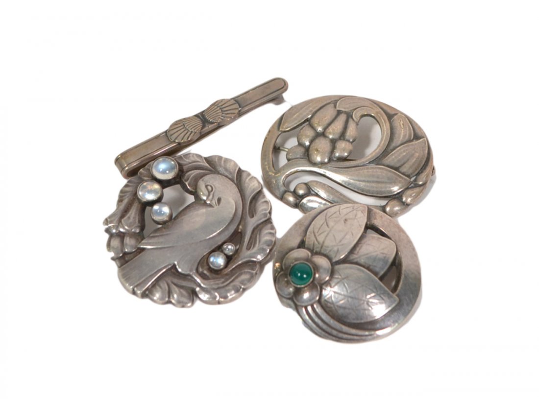 Four Gerog Jensen Sterling Pins: Comprises: 1.) Circular pin with preening dove and mounted with five small moonstones. 2.) Oval pin with foliate openwork decoration. 3.) Small circular pin with flower mounted with green stone. 4.) T