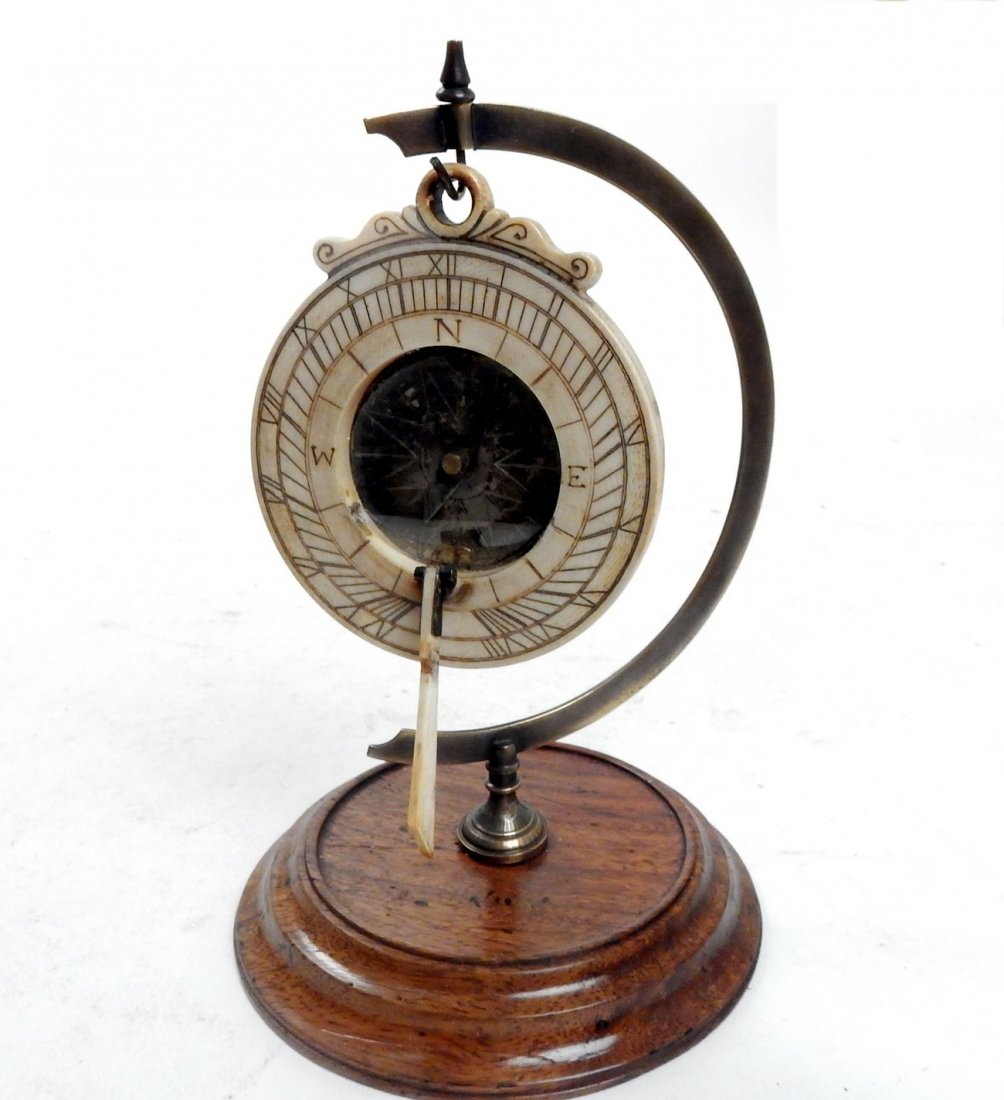 Scrimshaw Sundial on Wood Stand: Carved Scrimshaw sundial on a brass and wood stand. [4 1/2" x 7 1/4" H]. In good condition.