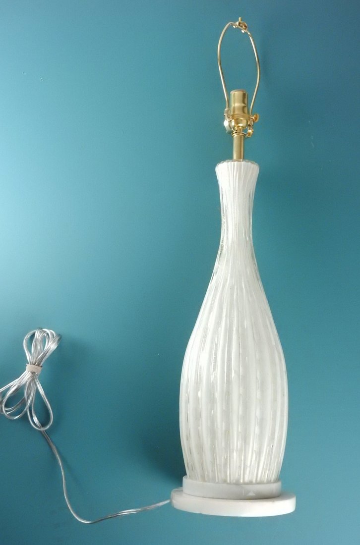 Single Mid-Century Modern Glass Lamp: Murano clear-over-white glass table lamp tapering toward top. Features vertical ribs, controlled air bubbles, and inclusive gold flecks. Bears a circular white marble base. [7 1/2" Dia at base x 27" H