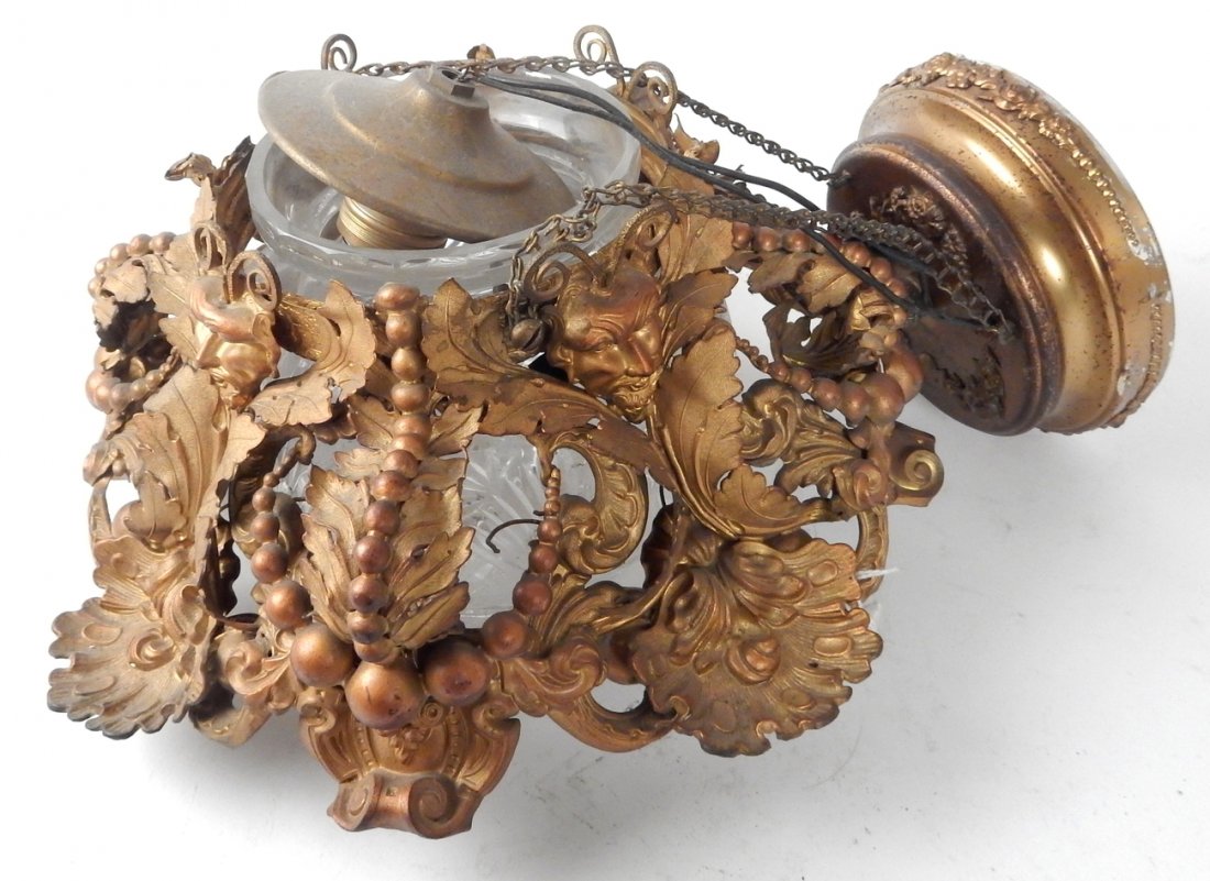 Gilt Bronze Light Fixture w/ Glass Shade: Baroque style gilt bronze with satyr masks and cut-glass shade. Ceiling fixture hangs from 3 chains. [Ceiling plate to globe: 16"; Fixture: 12" W x 6 1/2" H]. Good condition, some white paint on ceili