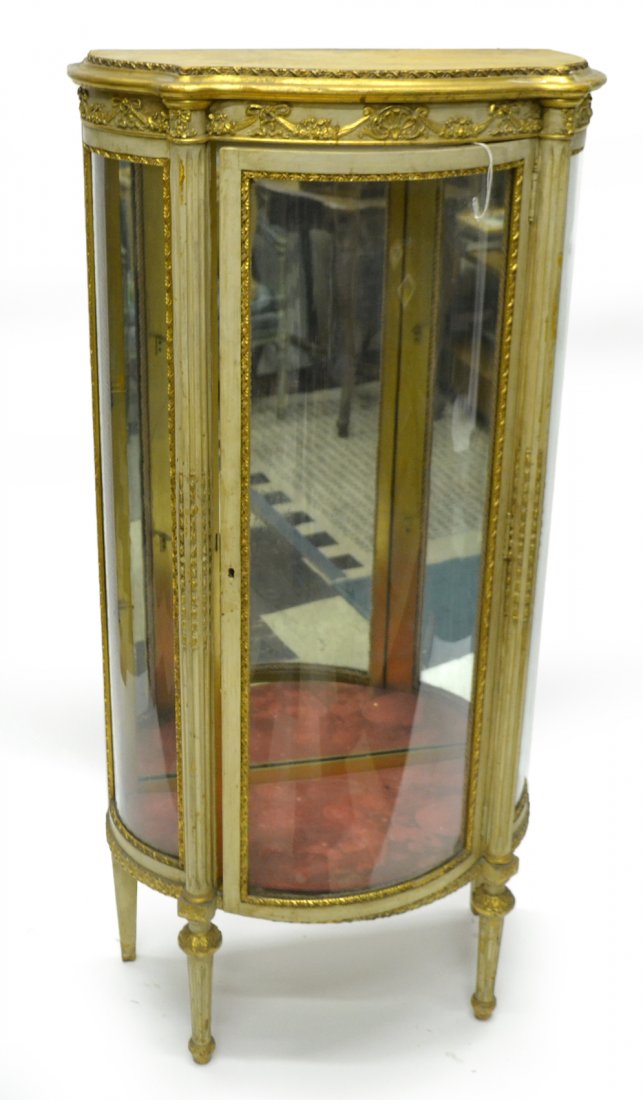 Louis XVI Style Painted Vitrine: Carved and painted curio cabinet with curved glass side and door. Bears a mirror back. Receives two glass shelves (not present). Missing escutcheon. [26 3/4" W x 13 1/4" D x 54 3/4" H]. Wear, with scu