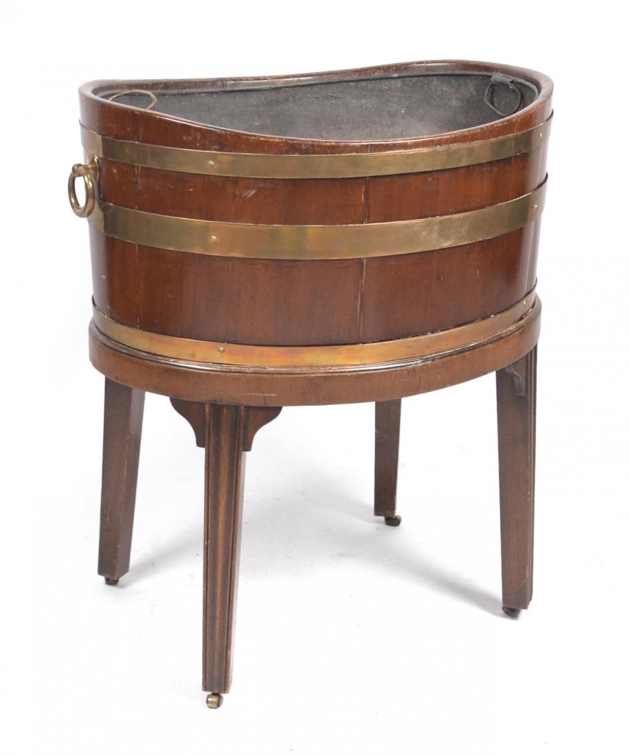 George III Style Oval Wine Cooler: George III style oval wine cooler having brass banding and lead liner. On a removable stand on brass casters. [24 3/4" W x 18 1/2" D x 27 1/2" H] Good condition, as with age.