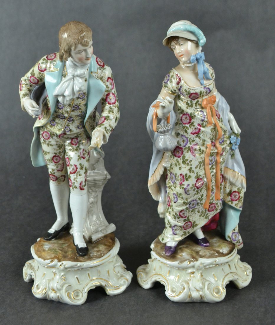 Pair of Antique Porcelain Figures: Pair of German-made porcelain figures. Woman and man, both in formal dress with floral motif, gesturing. Both bear mark on bottom. [4" Dia x 10 1/2" H]. Man has chipped finger, overall good condition.