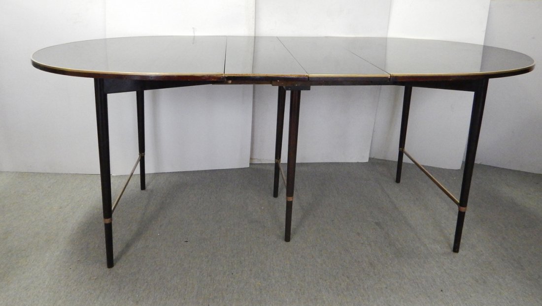 Modern Dining Room Table: Two-leaf elliptical lacquered table with brass perimeter and round, tapered legs. [62 1/2" W x 41 1/4" D x 29" H (without leaves); Each leaf 11" W]. Nicks, dents, and scratches.