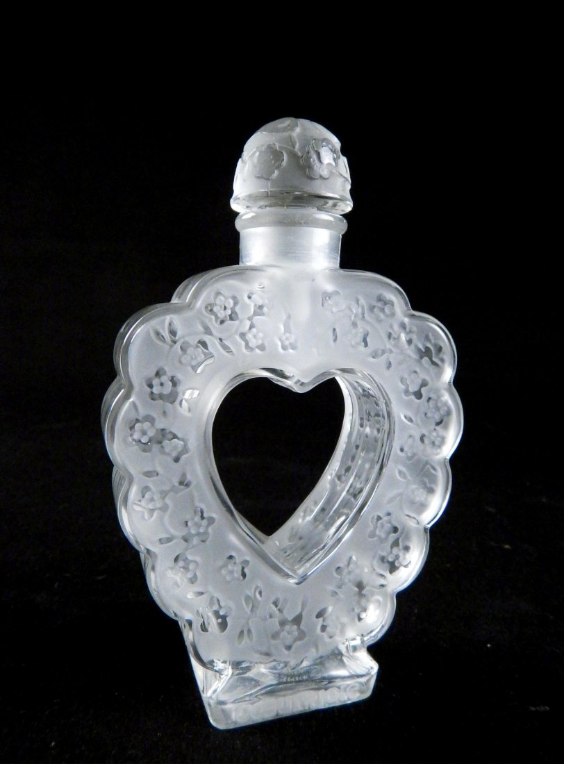 Lalique Heart-Form Perfume Bottle: Bottle with stopper. Heart-form perfume bottle with hollow center. Engraved "Loeur-Tolie" and "Nina Ricci" at bottom. [3 3/4" W x 1" D x 6" H]. Very light wear.