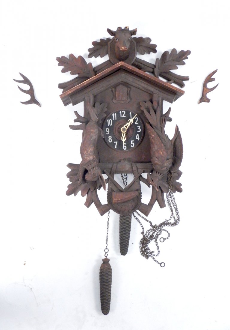 Vintage Black Forest Cuckoo Clock: Robustly carved clock with hunting trophy theme featuring a hare at left and fowl at right with crossed gun barrels below and a stag's head pediment. Bears two cast iron pine cone-form weights and oak