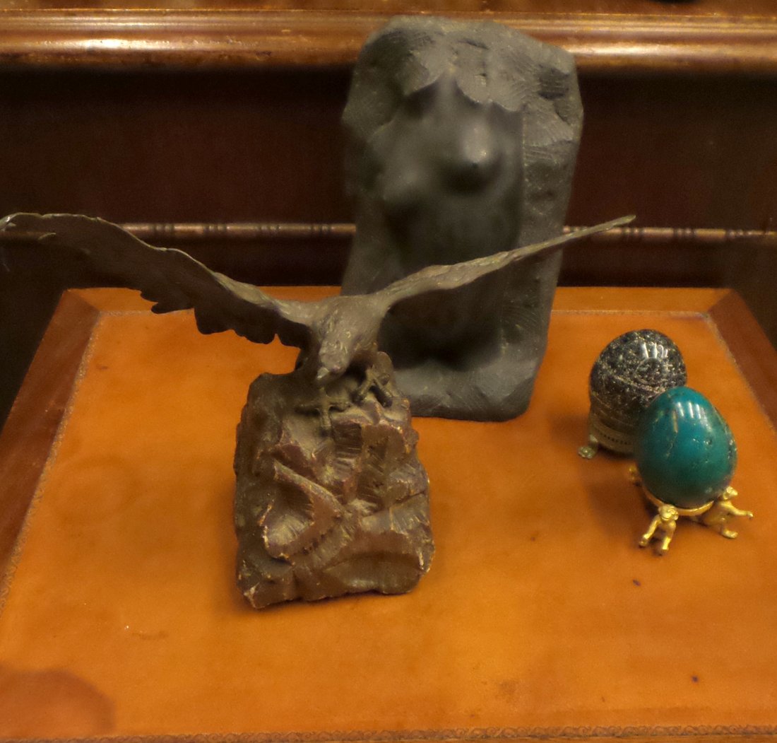 Four Assorted Table Ornaments: Comprising a bronze model of a spread-winged eagle on tinted stone base. Abrasions. [8" H x 10" W], a cast stone nude torso. [8" H]. and two decorative eggs on metal stands. One egg damaged.