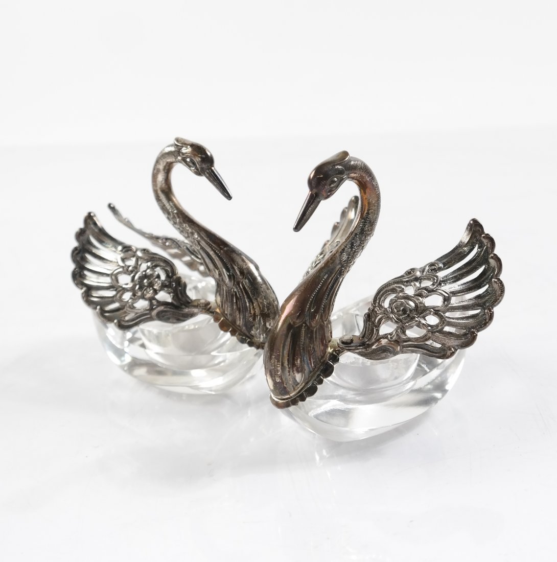 Pair of Swan-Form Salt Cellars: Pair of sterling and crystal swan salt cellars with repousse roses on wings. Includes a pair of salt spoons with cherub and roses motif. [3" W x 1 1/2" D x 2 5/8" H].